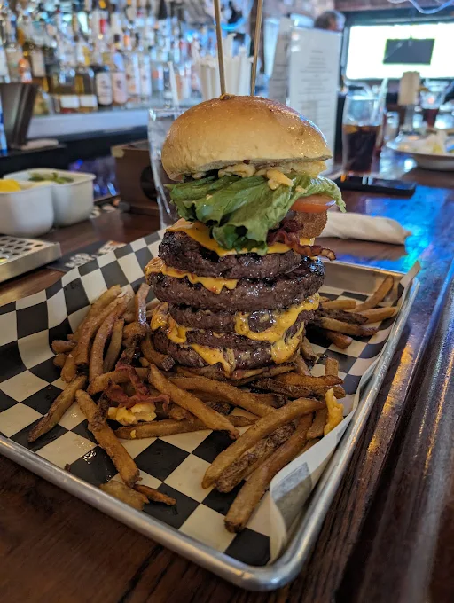 Towering multi-patty cheeseburger with hand-cut fries at the bar